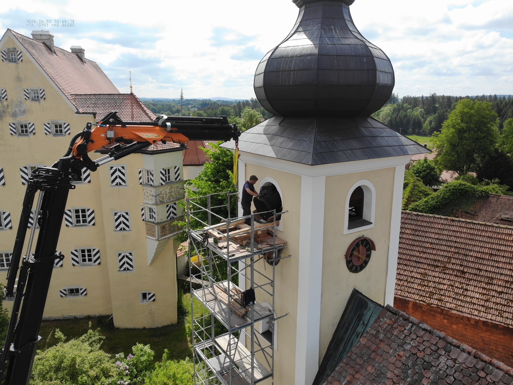 Bild zeigt den Ladekran von Herrmann & Wittrock vor dem Kirchturm in Thumsenreuth bei Krummennaab. Auf einem Gerüst stehen Mitarbeiter der Firma Bayreuther Turmuhren bereit, um mithilfe des Ladekrans die zwei alten Glocken herauszuheben, die ausgetauscht werden sollen.